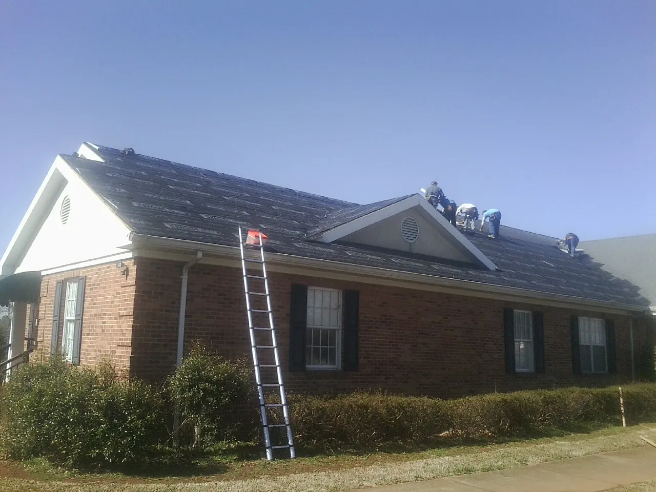 Crew tearing shingles off a brick ranch roof with a ladder set — Metal Roof Repair work by our crew in Pasco