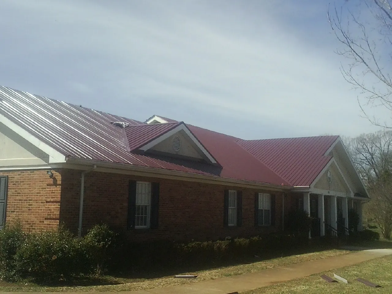 Red metal roof with gabled entries on a long brick building, from a Hail Damage Roof Repair job in Pasco